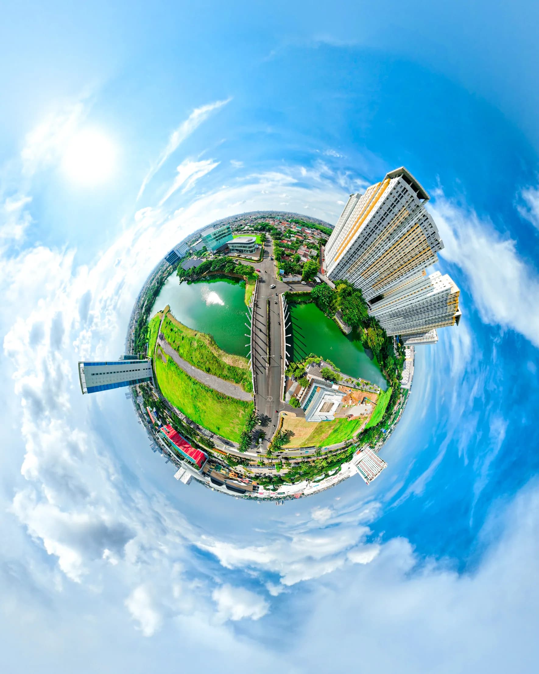 A creative aerial perspective showcasing modern architecture, a striking high-rise building, and a surrounding landscape shaped into a unique little planet composition. The panoramic view highlights the contrast between urban development, green spaces, and reflective waterways beneath a vibrant blue sky, delivering a distinctive visual experience through creative aerial photography.